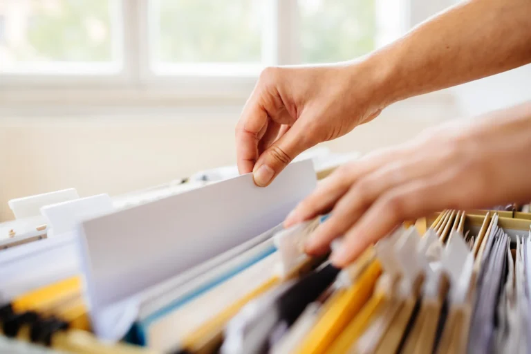 Hands search for documents in suspension files in a filing cabinet