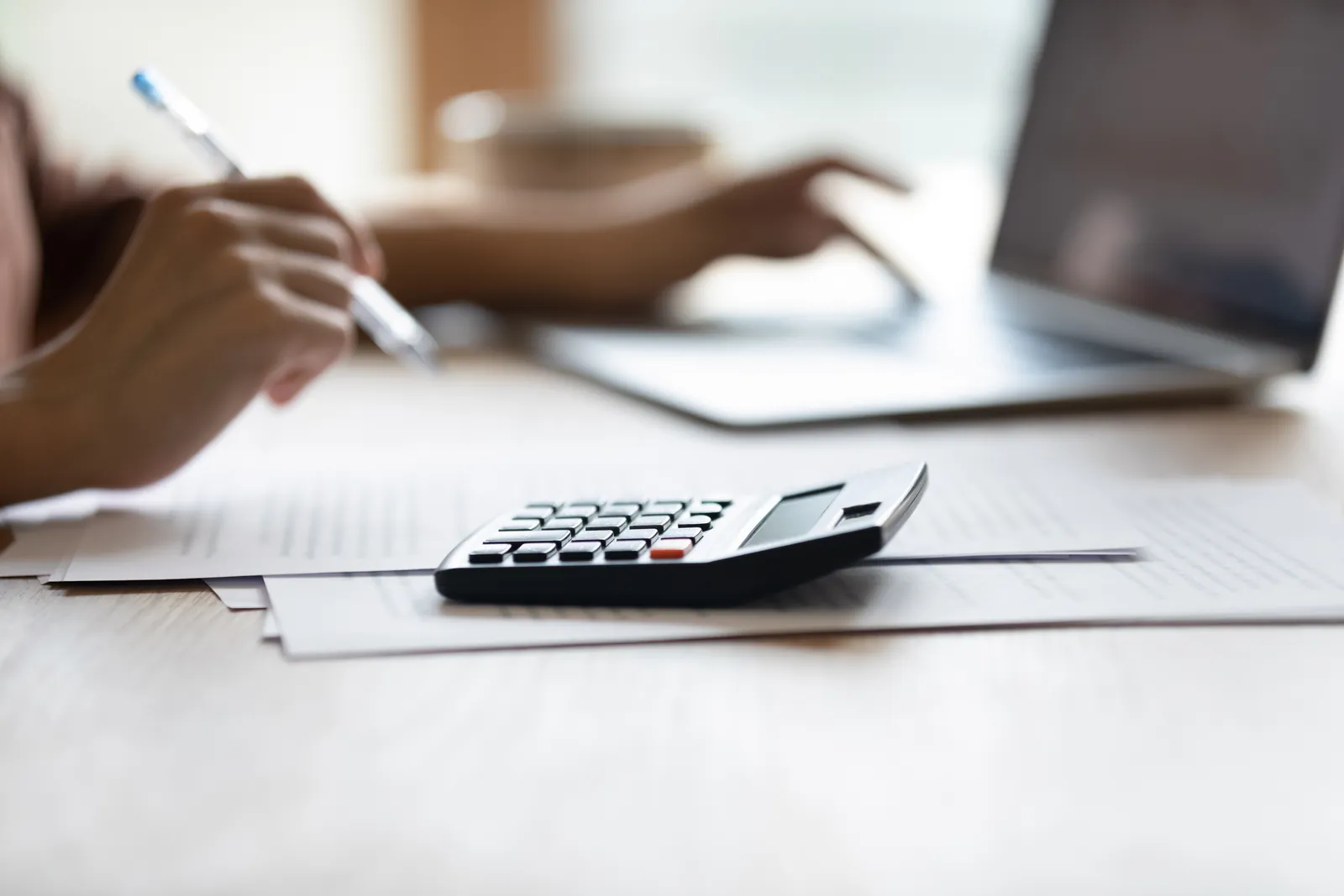 Hands with financial documents, a calculator and a laptop