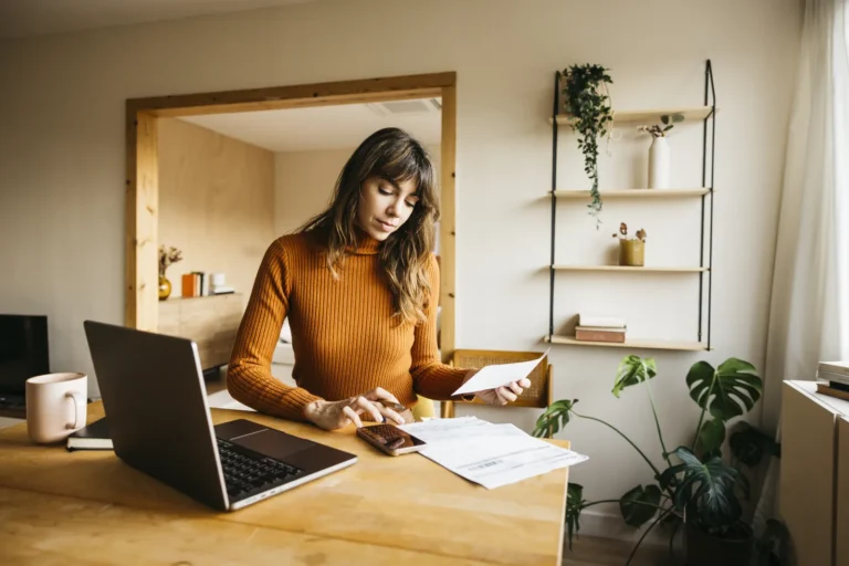 Woman checks an invoice with her laptop and phone at a desk