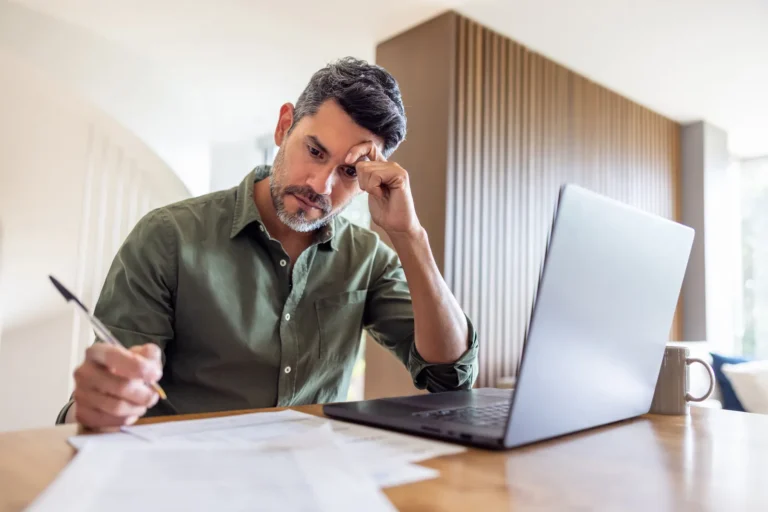 Man bekijkt documenten aan zijn bureau naast een laptop
