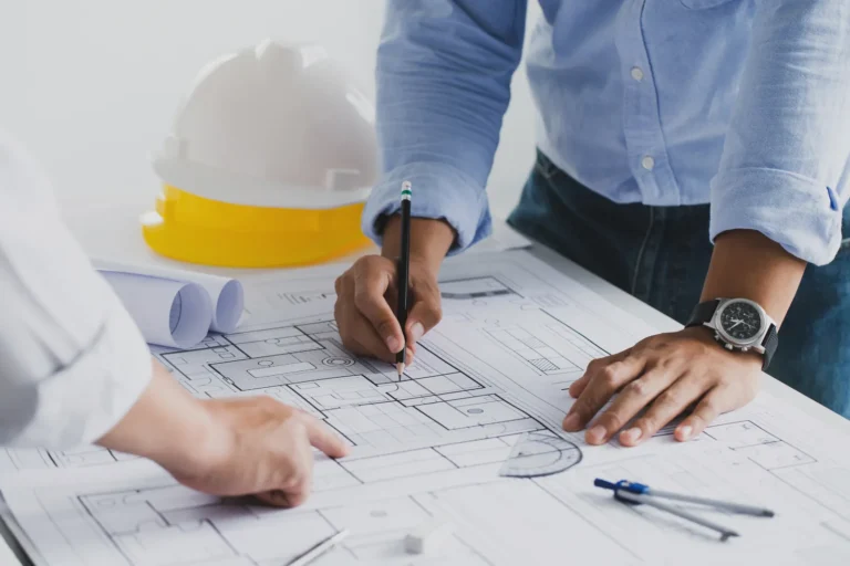 Two people are discussing a construction drawing at a desk